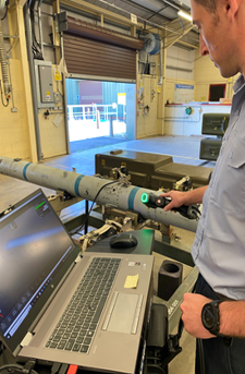 A person using a handheld scanner on a missile in a hangar